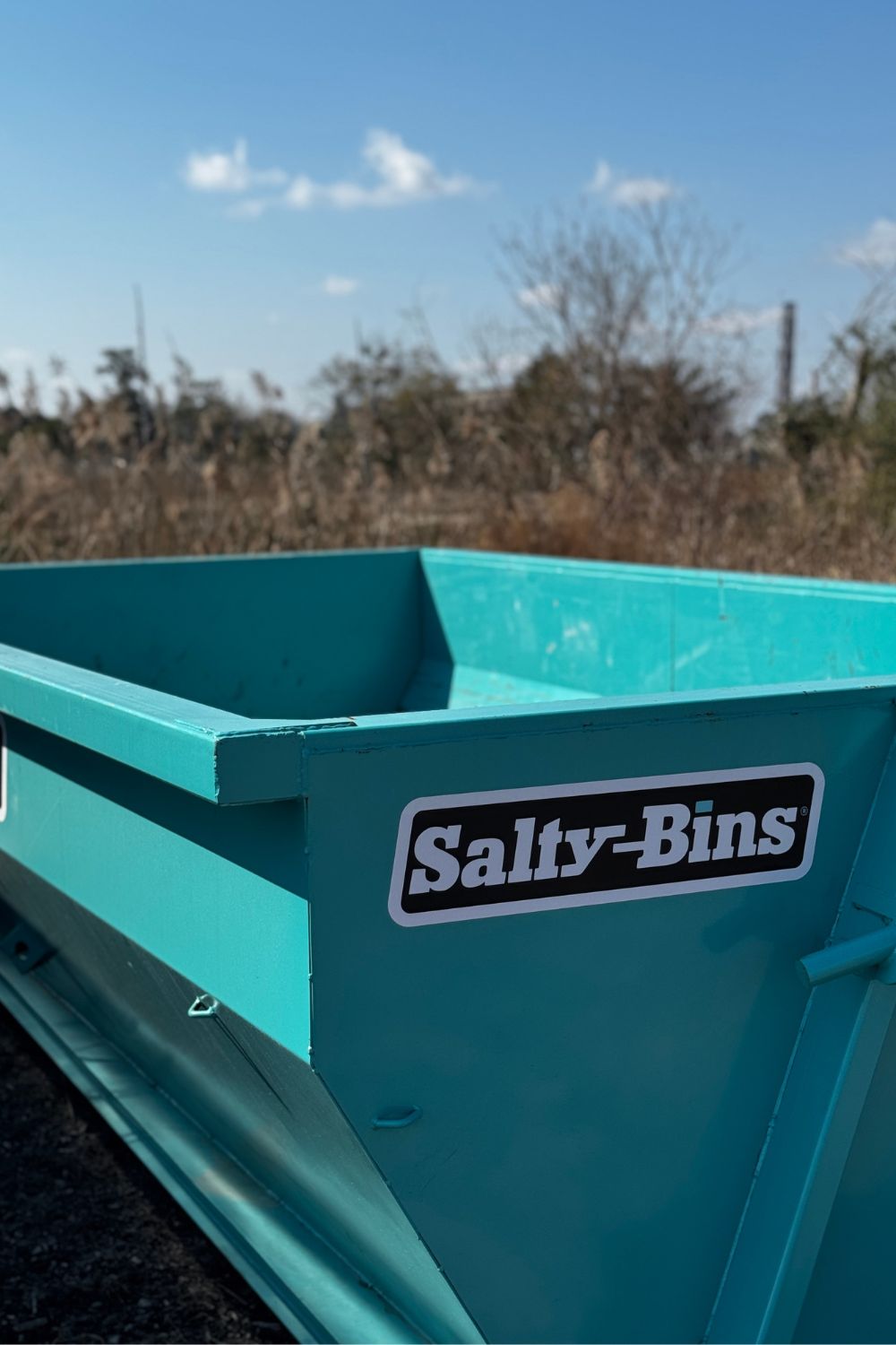 Teal steel dumpster in Wilmington NC with landscape in the background,