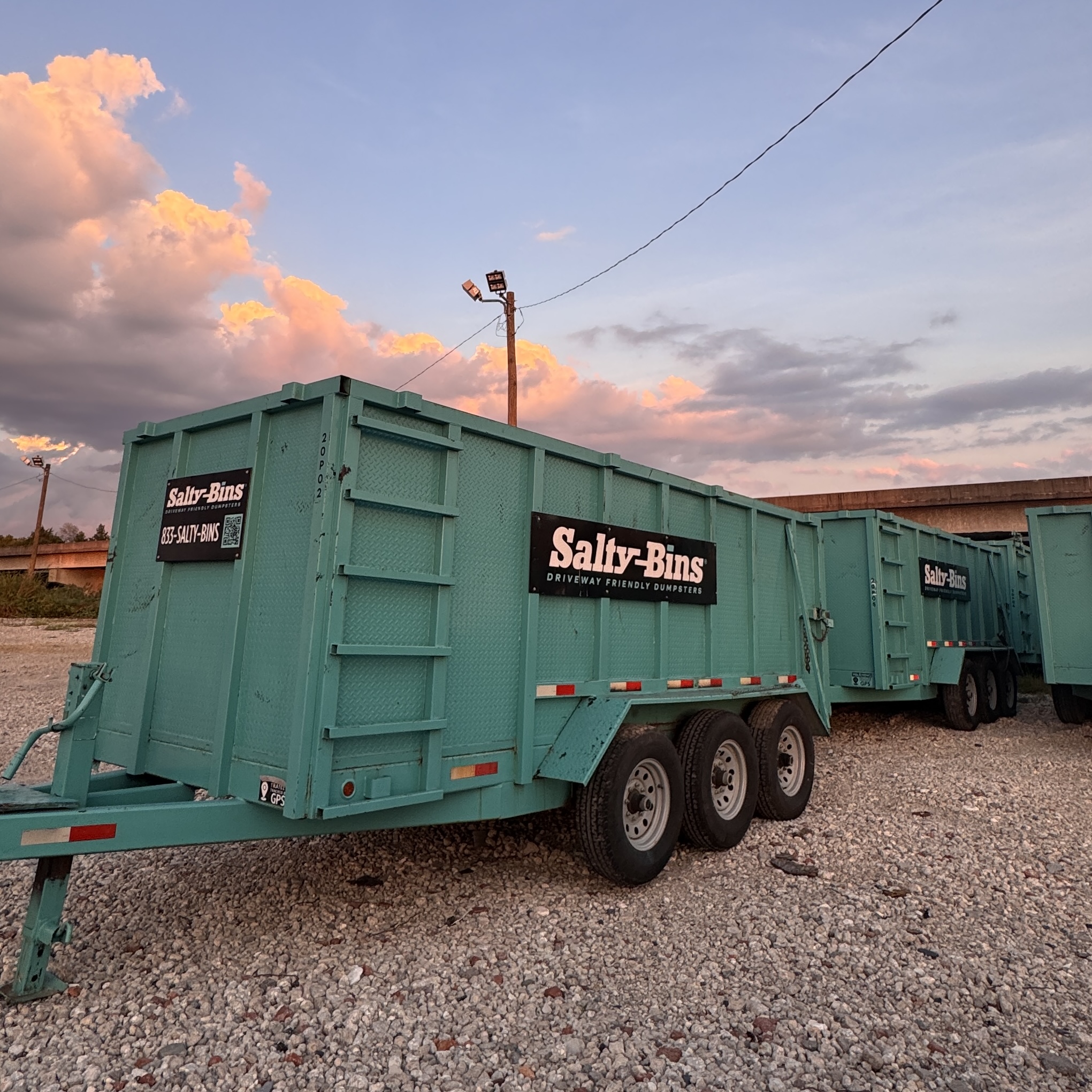 Salty Bins 20YD Premium Driveway Dumpster on wheels, in their signature teal color. Placed on a gravel lot in Wilmington, NC